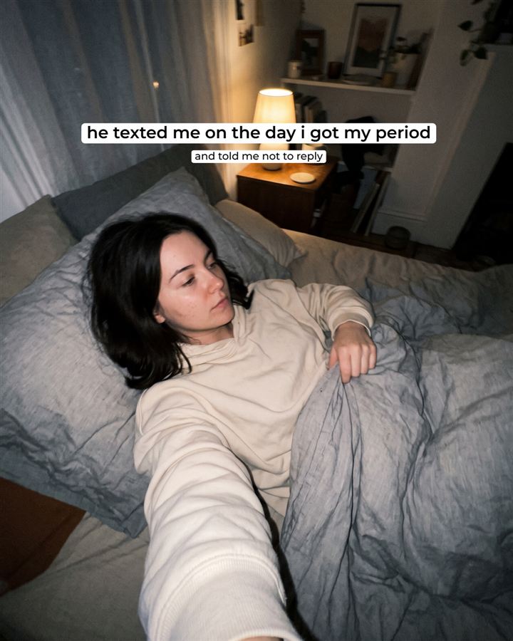 A candid phone selfie of a woman lying in bed in a dim room at night. Text over it: 'he texted me on the day i got my period', and under that, 'and told me not to reply'.