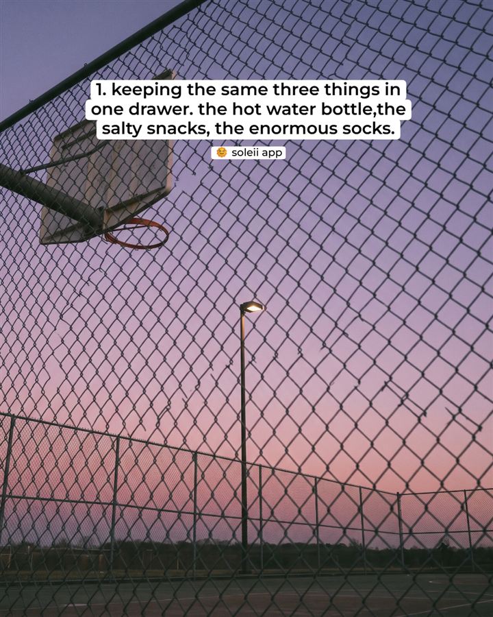 An empty basketball court at dusk behind a chain-link fence. '1. keeping the same three things in one drawer. the hot water bottle, the salty snacks, the enormous socks.' A small 'soleii app' pill sits underneath.